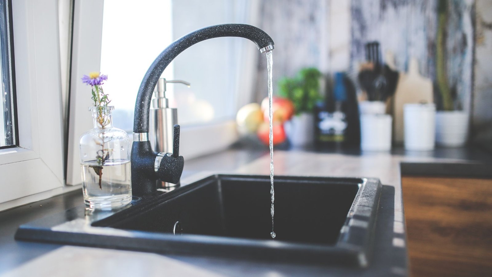 How to choose a whole house water filter featuring black kitchen sink with running water and flower.