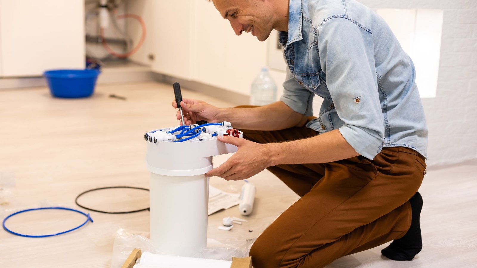 Reverse osmosis plumbing repair depicting man fixing filter unit, tool in hand, home setting.