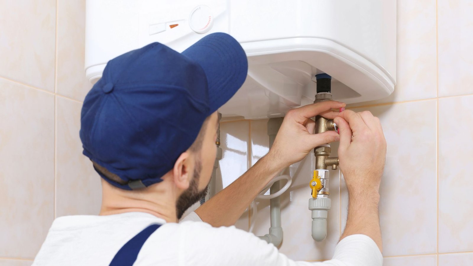 Water heater plumbing maintenance technician adjusting pipes in a clean, well-lit bathroom setting.