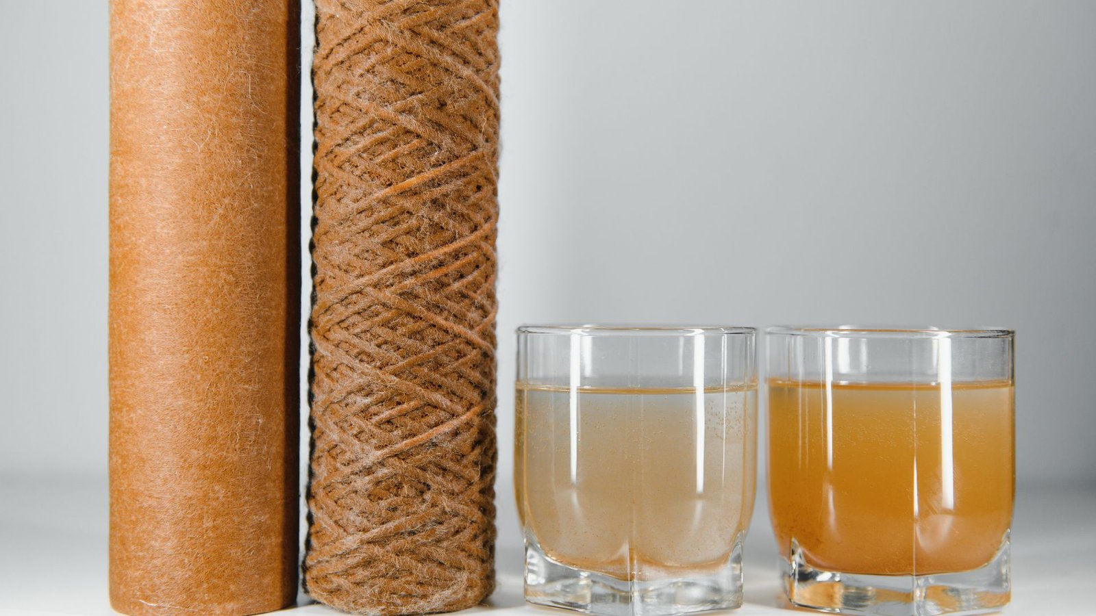 Best whole house water filters showcasing used filters and contrasting water quality in two glasses.