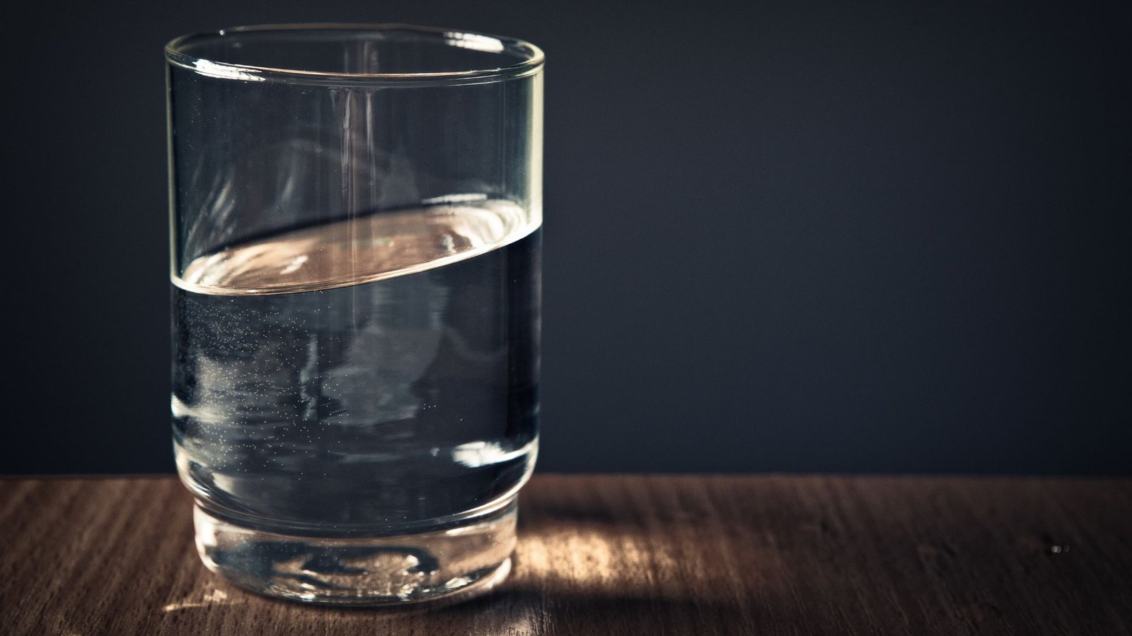 Chloramine removal half-full glass of water on wooden surface with dramatic lighting and reflections.