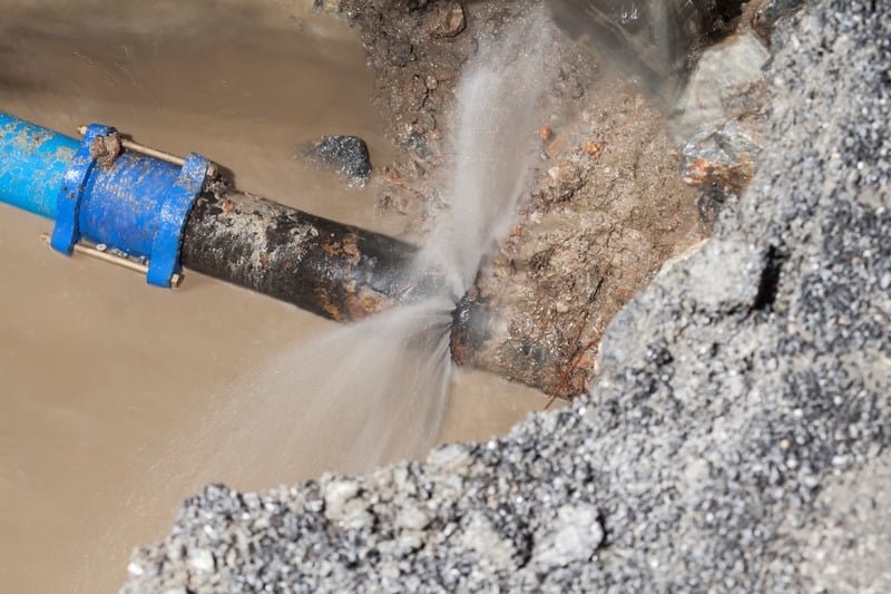 Iron removal well sprouting burst water pipe outdoors causing erosion and muddy accumulation.