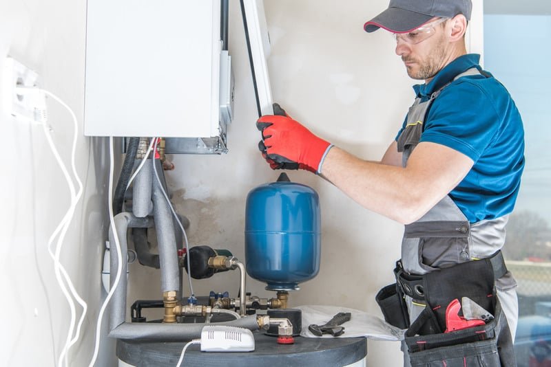 Tankless Water Heater Worker servicing complex plumbing system with valves, pipes, and pressure tank.