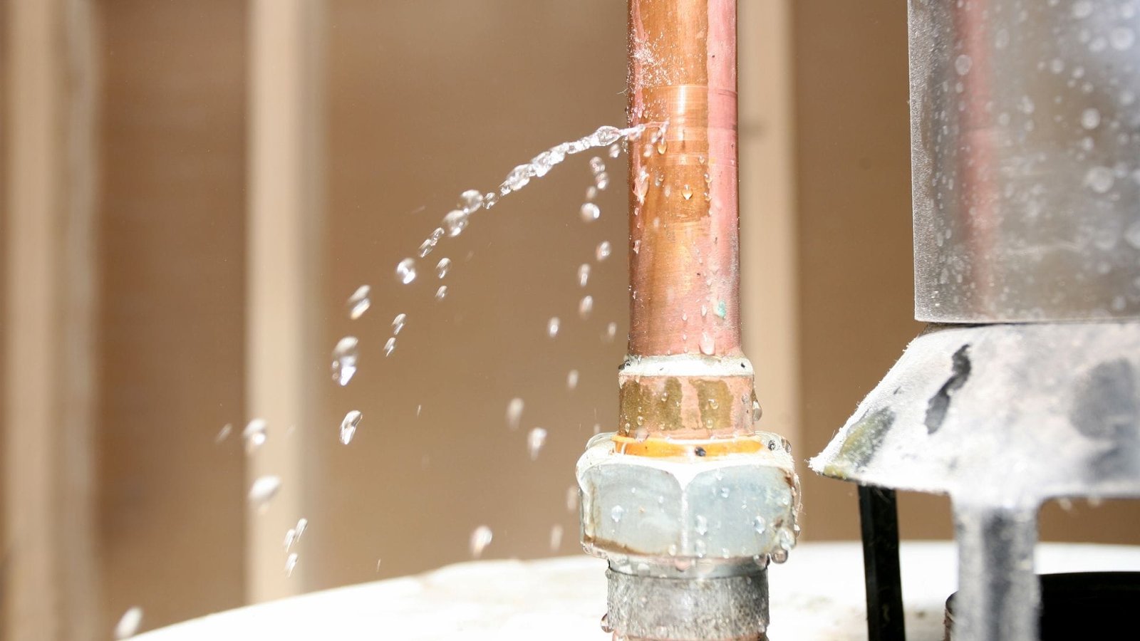Water softener leaking: close-up of a copper pipe spraying water, requiring urgent plumbing repair.