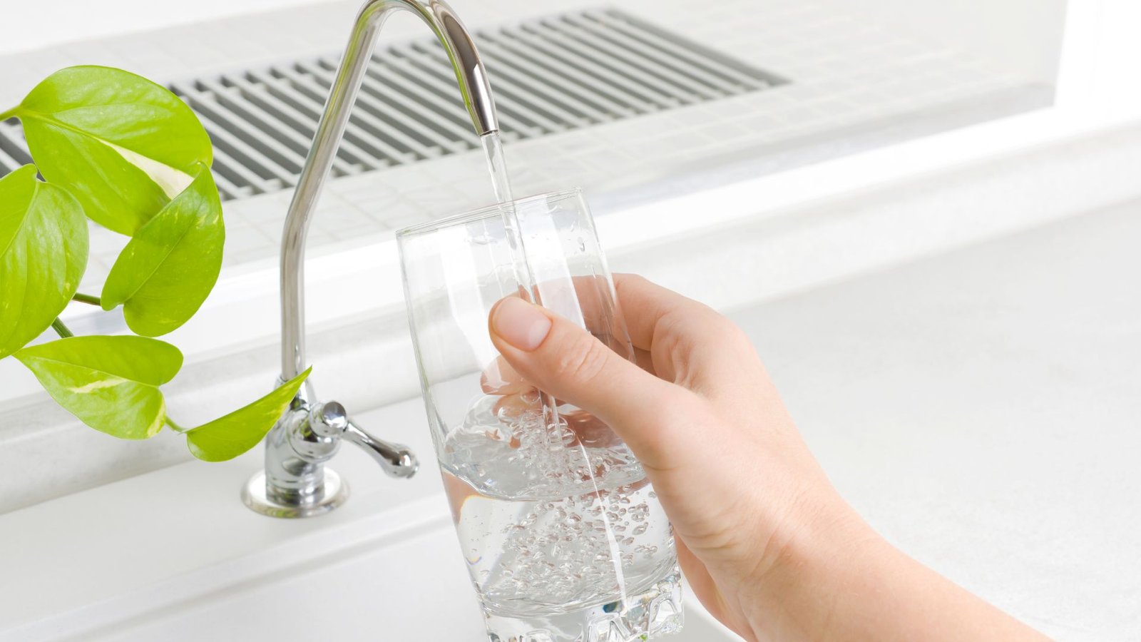 Chloramine removal modern kitchen scene with clear water flowing into a glass by metallic faucet.