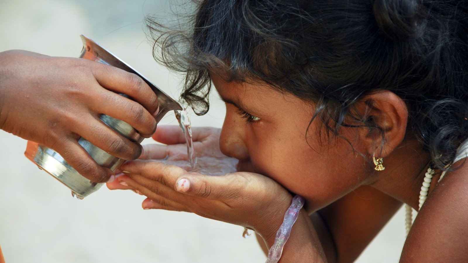 Home water testing scene with child drinking from cupped hands as water is poured from a metal cup.