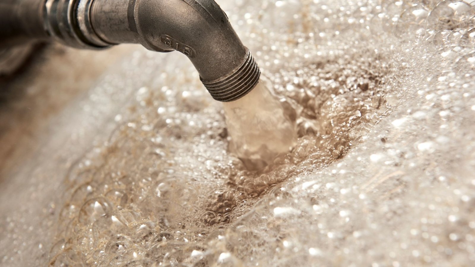 Home Water Testing: Steel pipe with water flow creating dynamic frothy bubbles under diffused light.