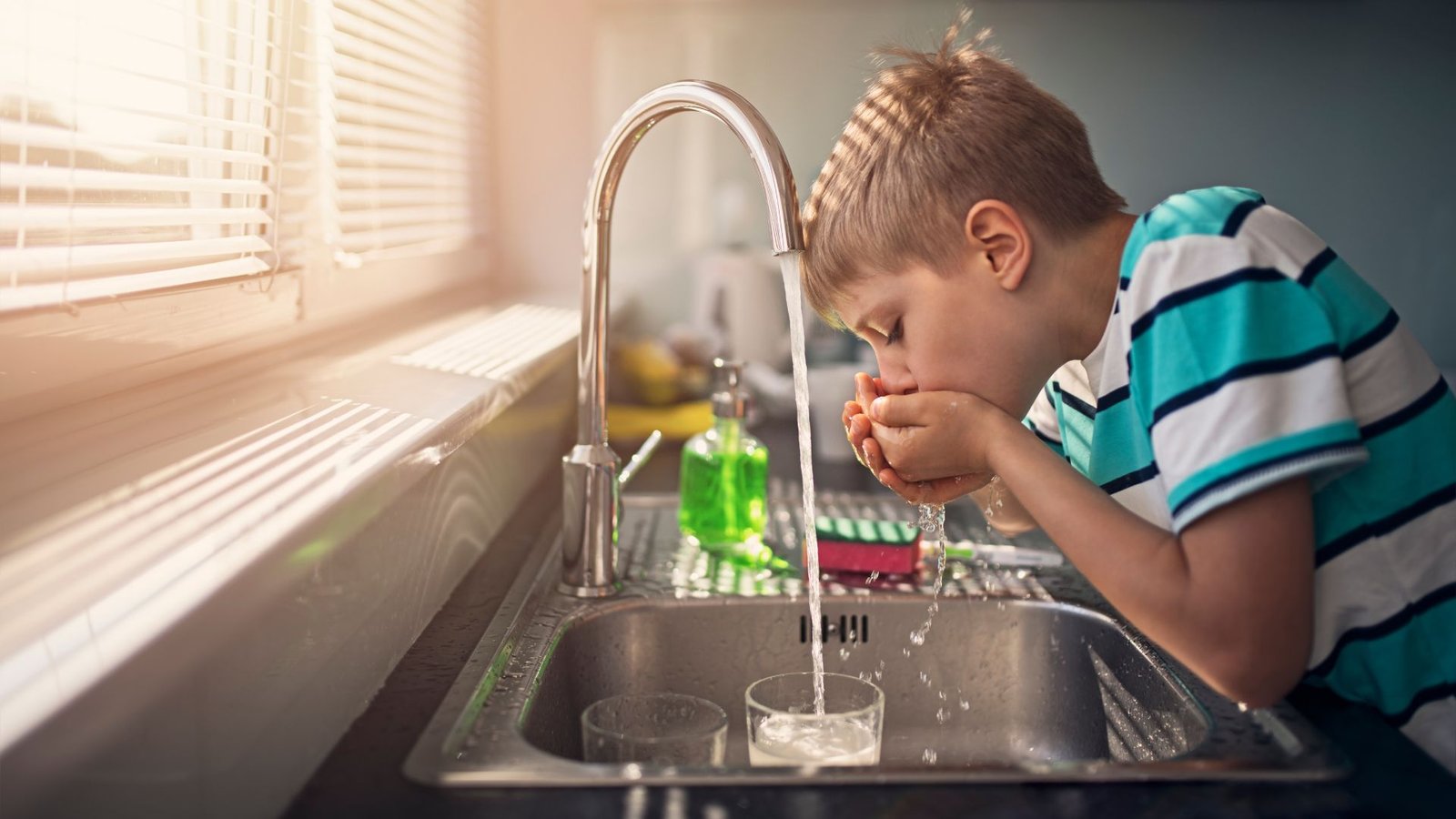 Reverse osmosis vs distilled water boy drinks from kitchen tap in bright modern setting.