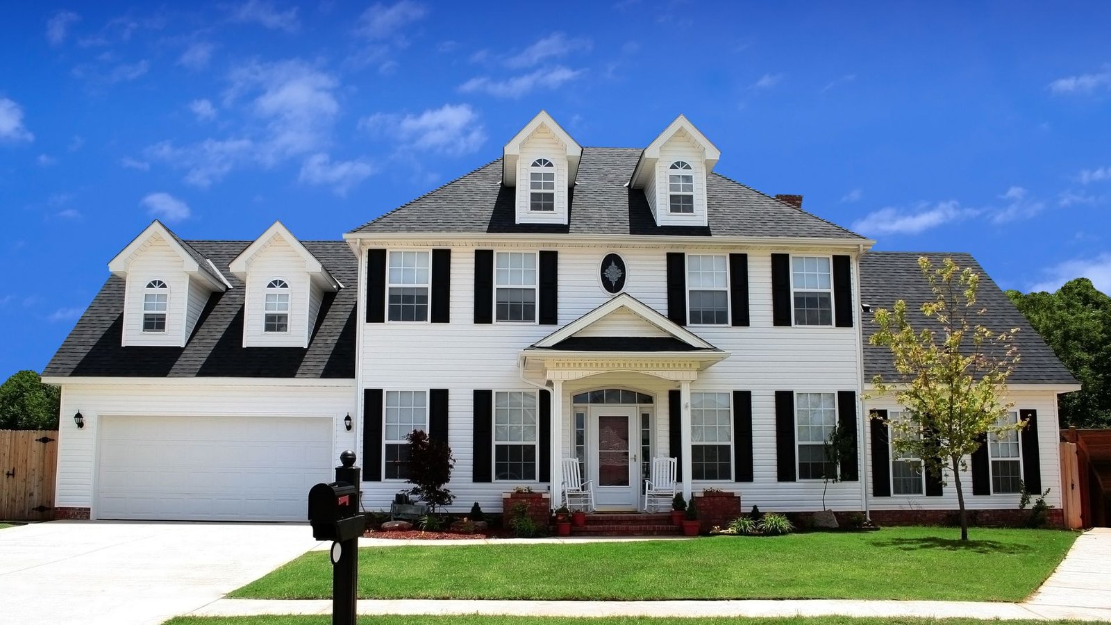 Charming two-story suburban home with white facade and black shutters, featuring gabled roofs and manicured lawn.