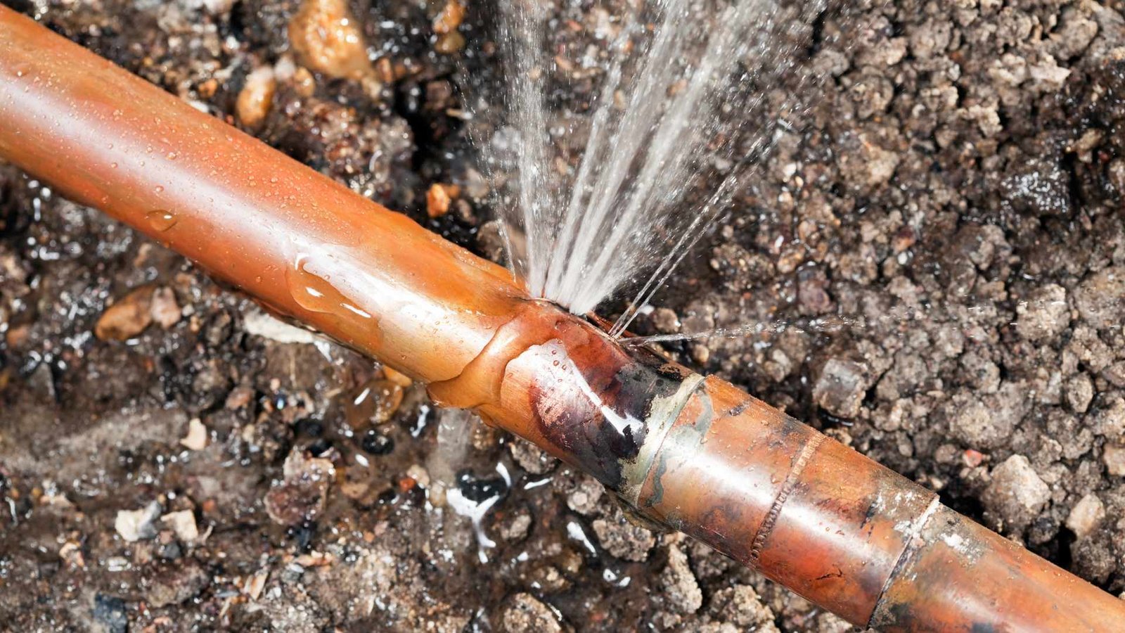 Water bills broken copper pipe spraying high-pressure water in gravel soil, highlighting urgent repair need.