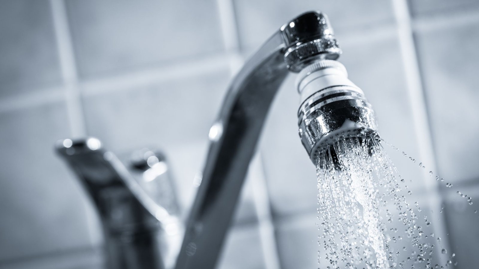 Water bills modern faucet highlighting chrome design with steady water flow on gray tile backdrop.