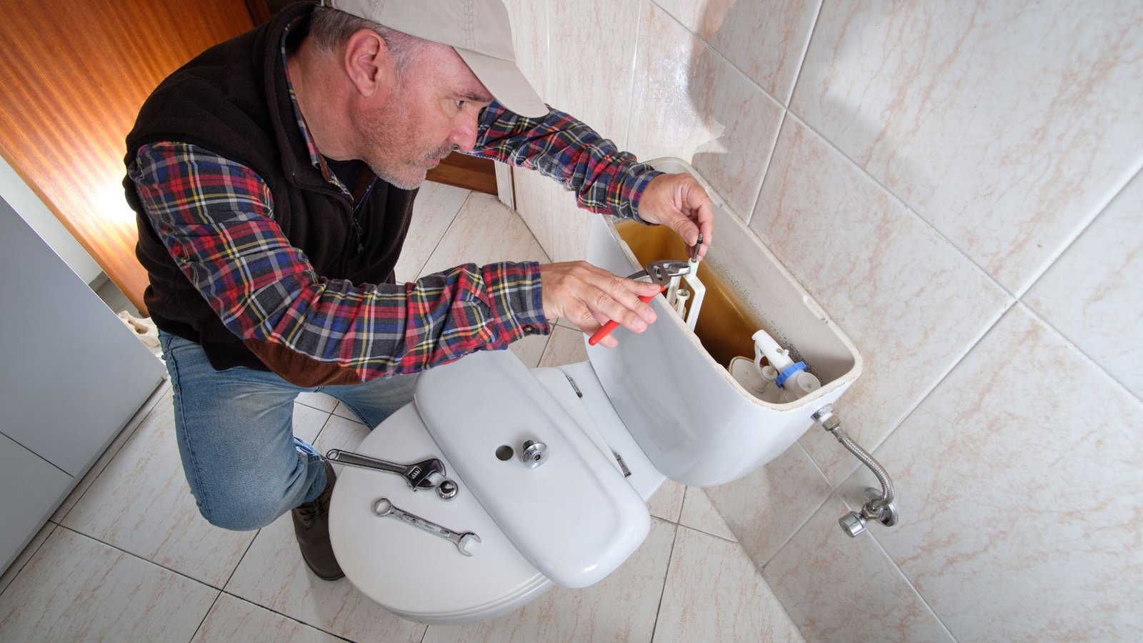 Water bills solution: Man repairing toilet tank in clean bathroom with tools, enhancing plumbing efficiency.