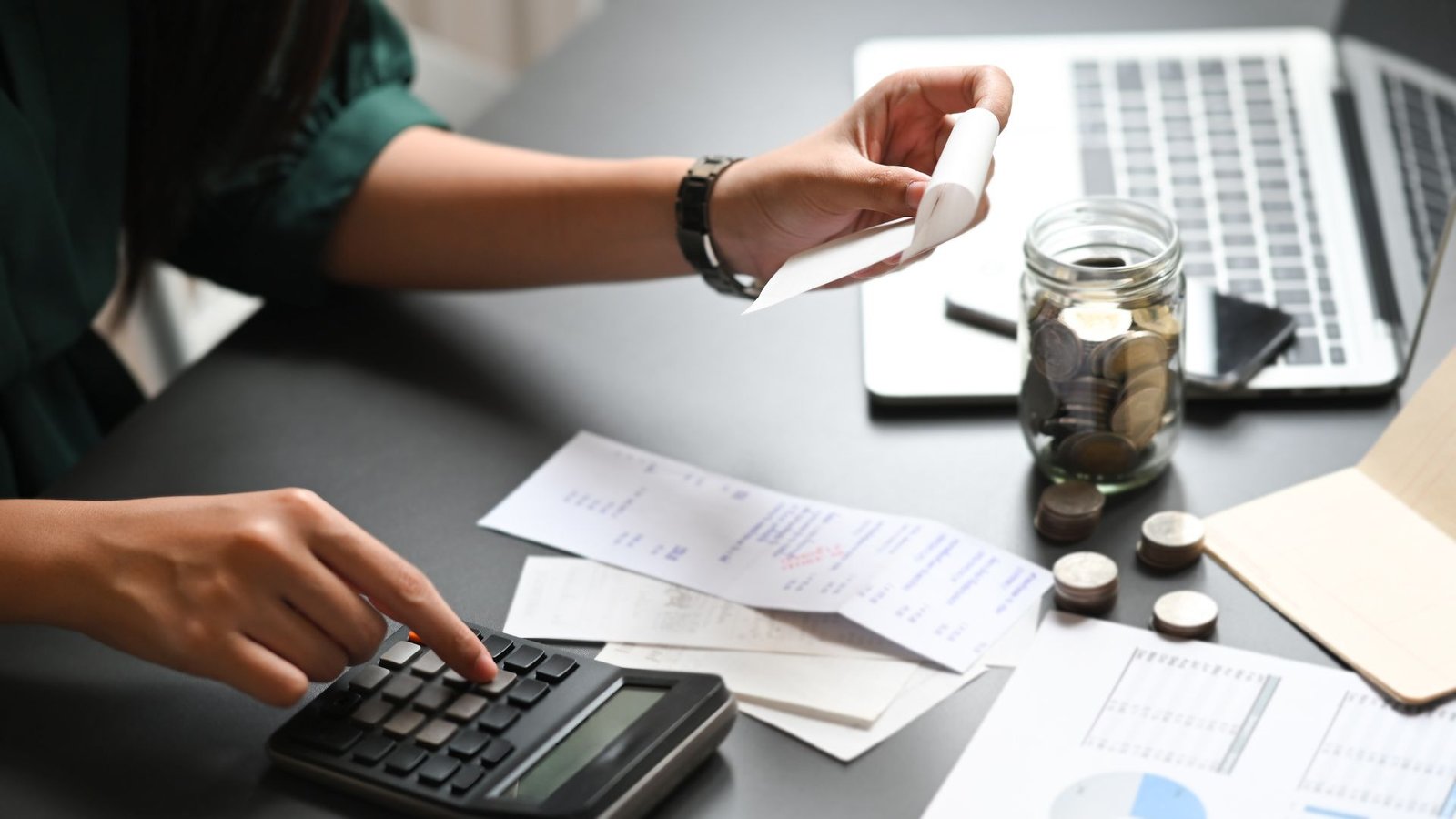 Apartment water softener financial desk setup with calculator, receipts, savings jar, and laptop.