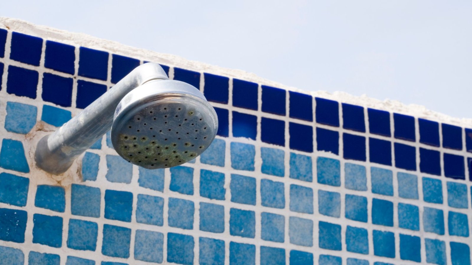 Best Water Softeners feature a polished metal outdoor showerhead amidst blue mosaic tiles under open sky.